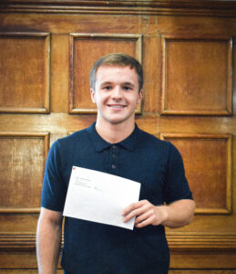 Smiling student holding A Level Results 