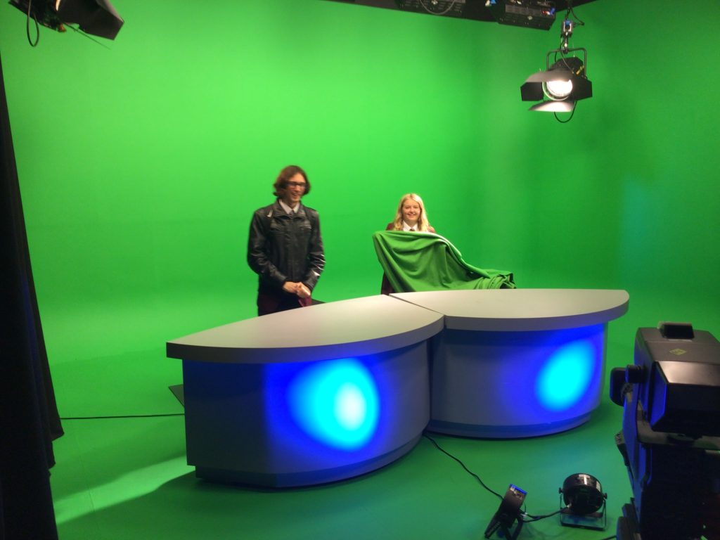 Two students from Hazel Grove High School stand behind a presenter's table in a greenroom.