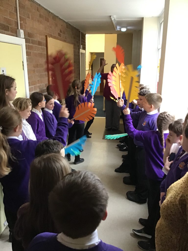Children waving cardboard palm leaves while stood in a corridor