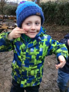 Child with coat and hat on wiping muddy hands on face