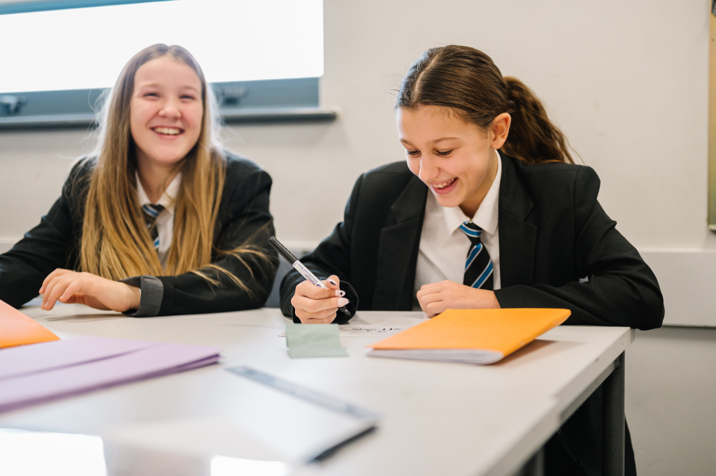 Jack Christophers smiling towards pupil with pen in hand.
