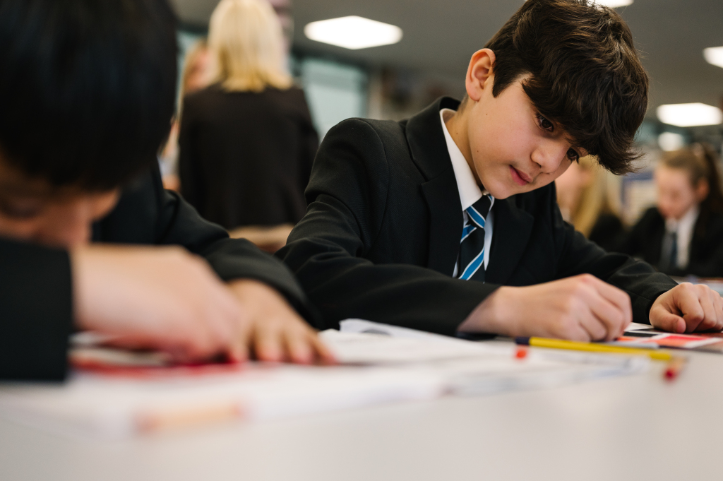 Jack Christophers smiling towards pupil with pen in hand.