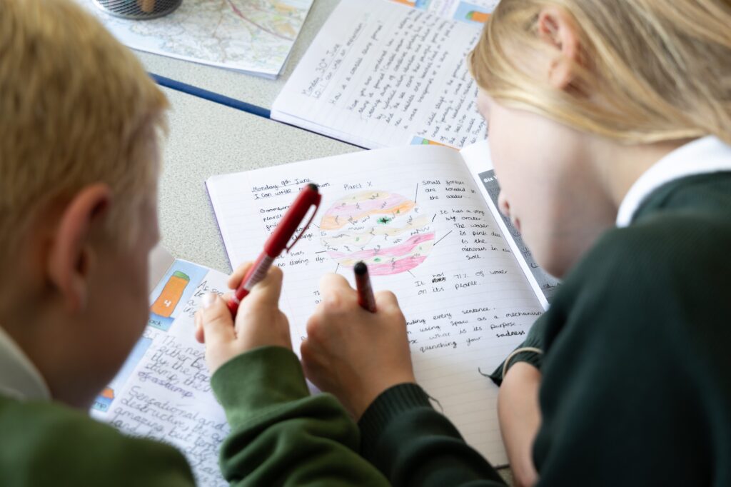 Two pupils at Norris Bank Primary hold pens and focus on their work during a lesson.
