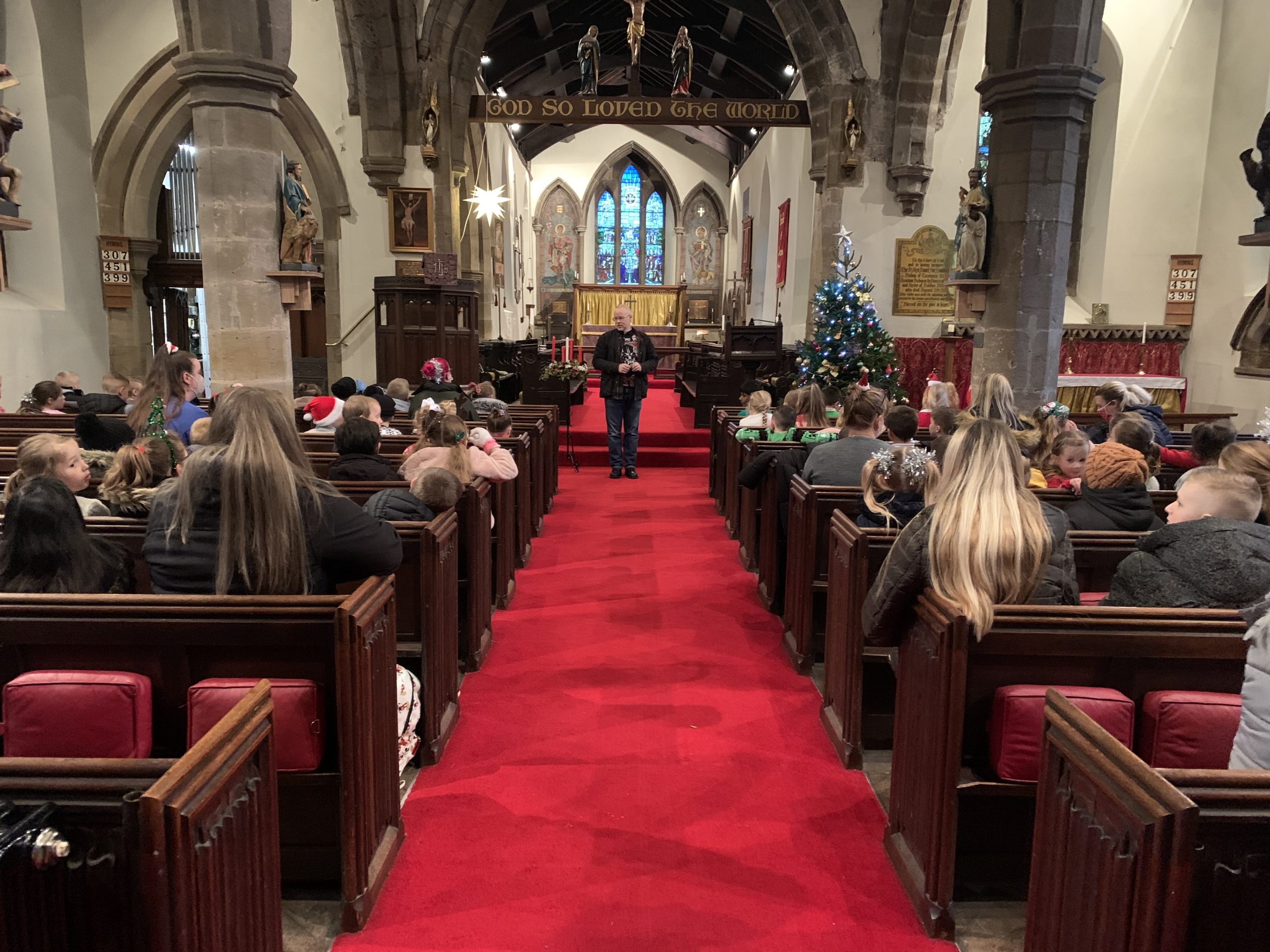 KS1 children and adults listening to Rev Paul in the church