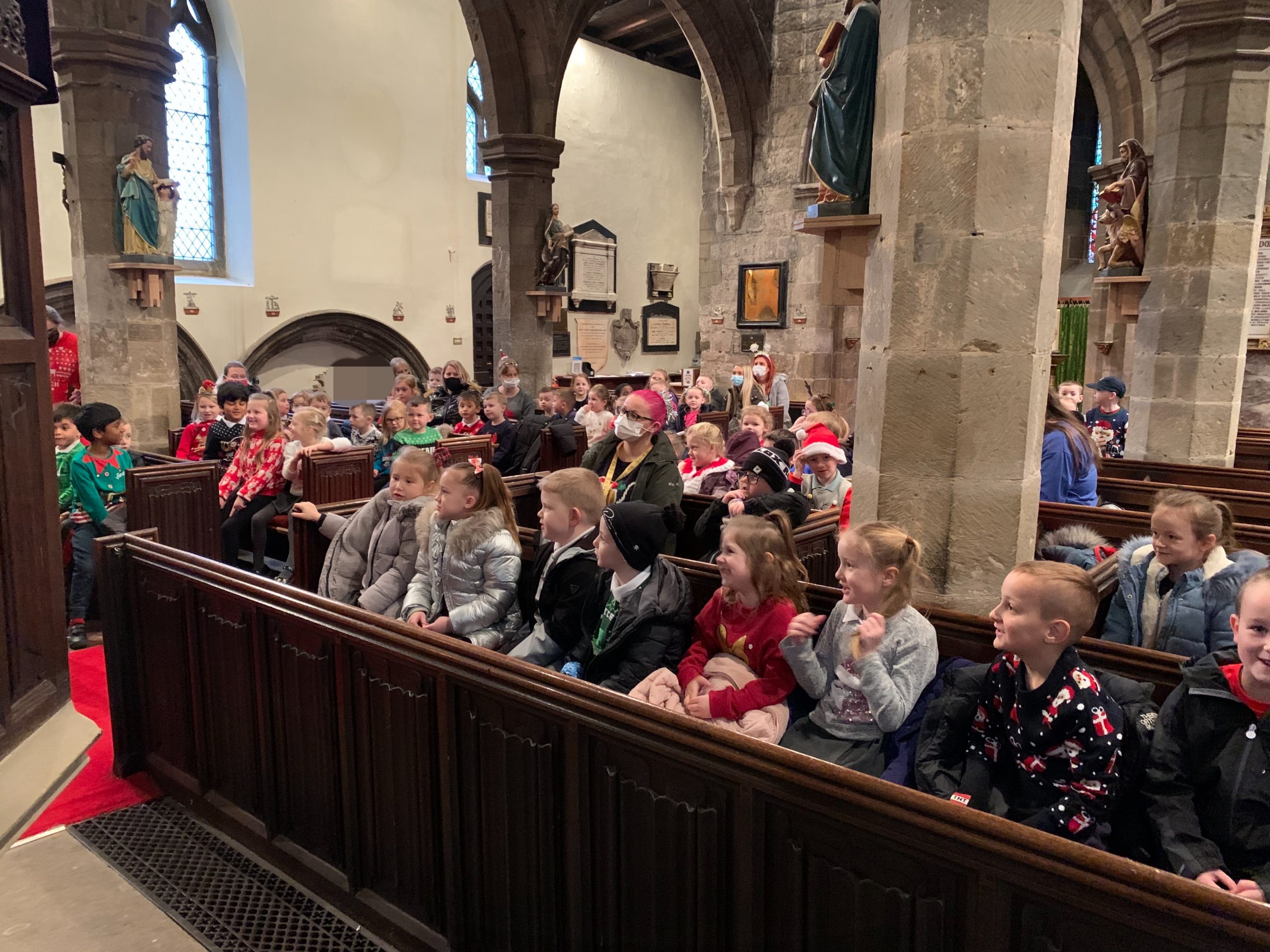 KS1 children and adults listening to Rev Paul in the church