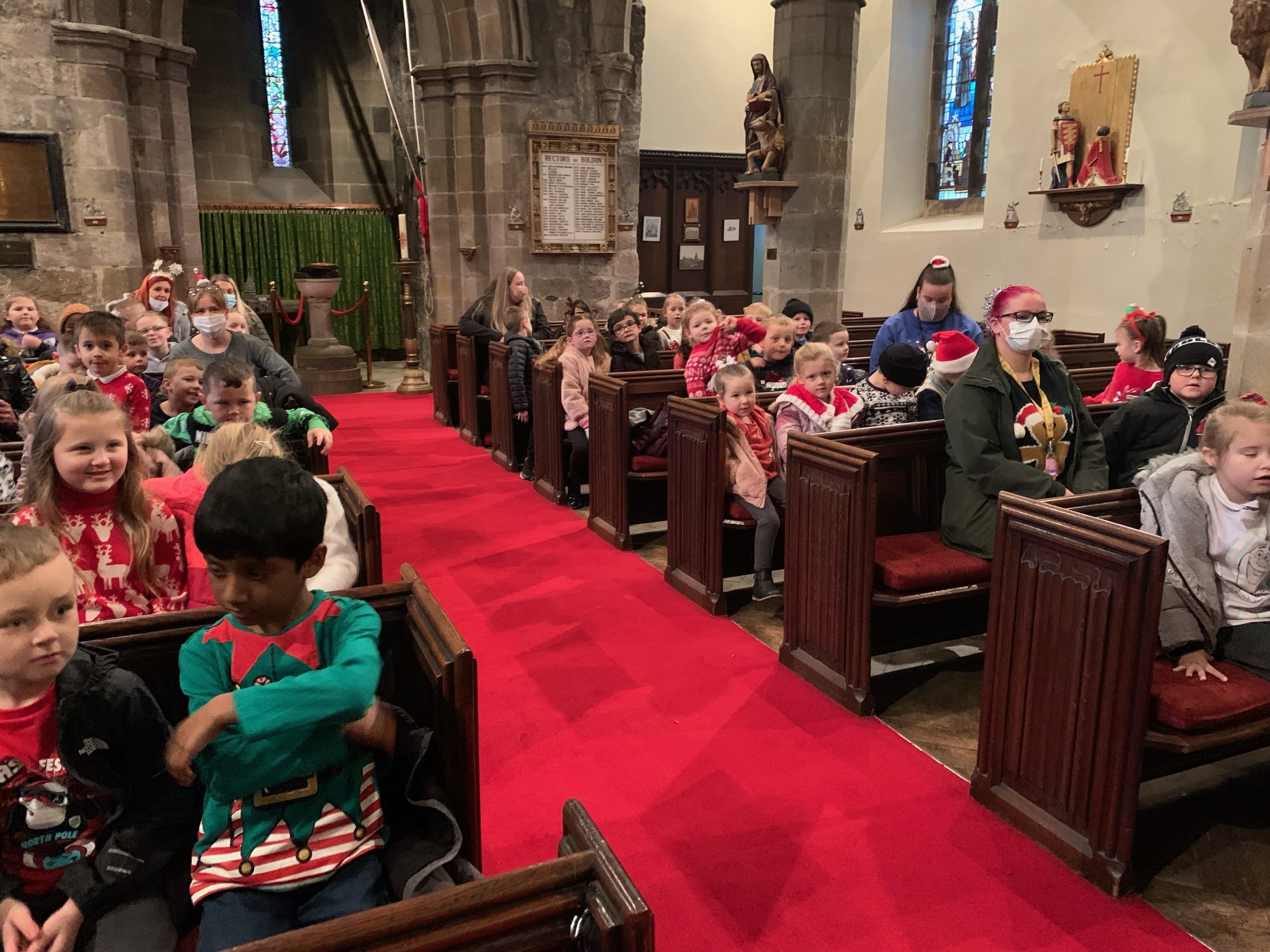 KS1 children and adults listening to Rev Paul in the church