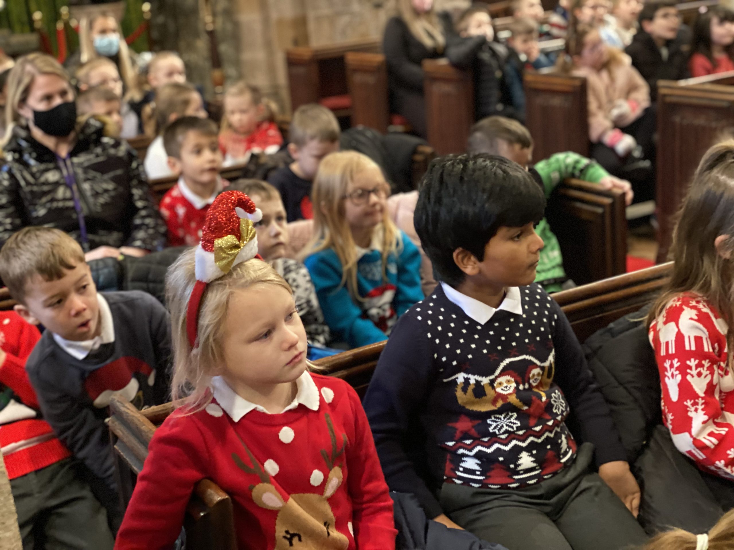 KS1 children and adults listening to Rev Paul in the church