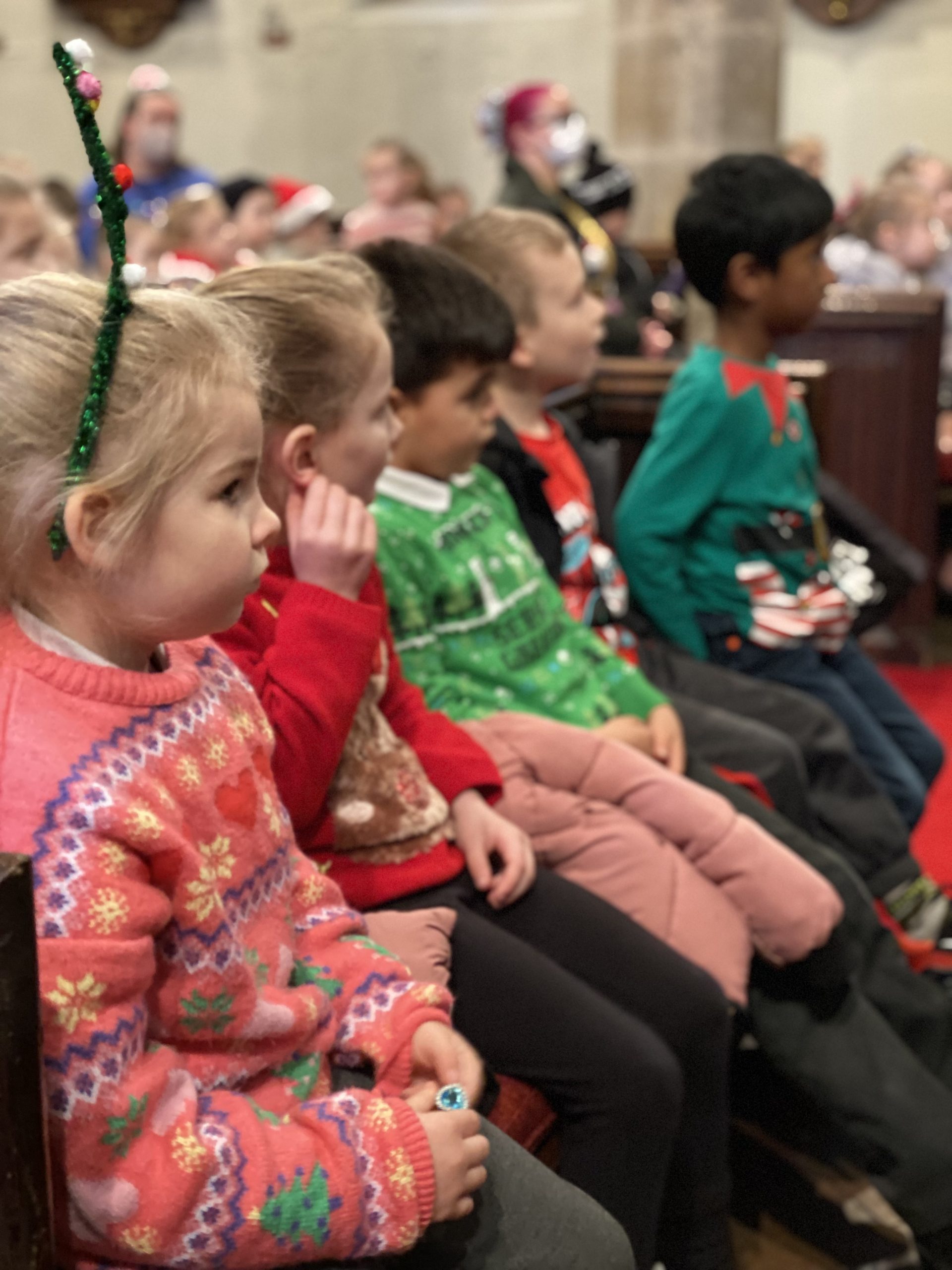 KS1 children and adults listening to Rev Paul in the church